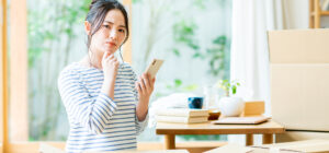 pixta 66858574 M 汚部屋掃除の料金がどのくらいかかるか悩む女性